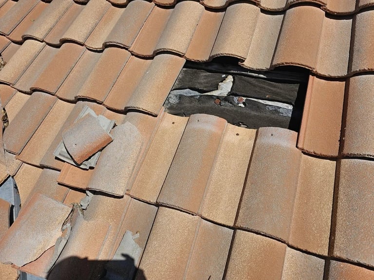 Damaged roof with broken terra cotta tiles and exposed dark underlayment showing water infiltration issues