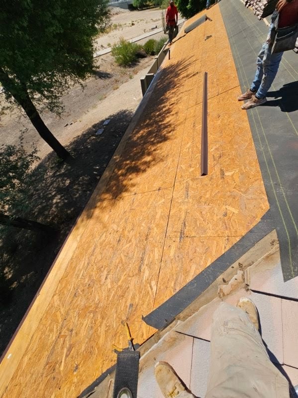 Overhead view of roof installation with yellow oriented strand board sheathing, black underlayment, and workers on the roof structure